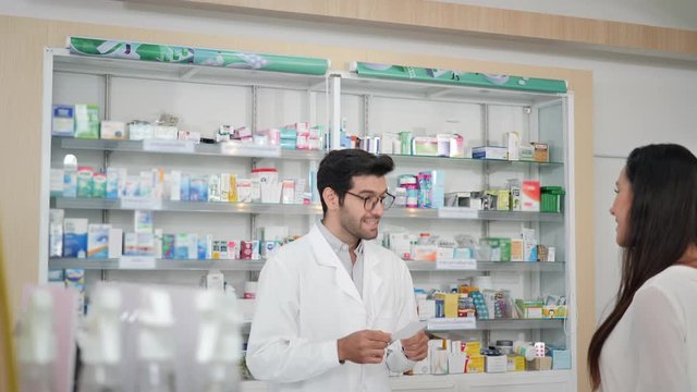 Middle eastern male pharmacist selling medications to woman patient and making drug recommendations in modern pharmacy