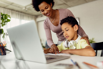 Happy African American mother assisting her son in homework.