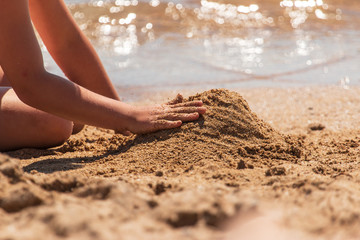 children's hands build a sand castle on the beach
