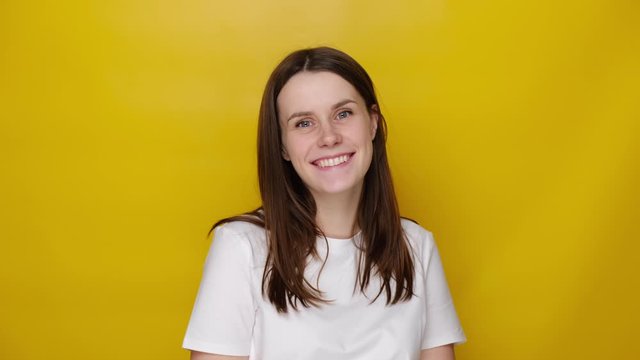 Portrait of cute millennial woman looking at camera laugh feels happy, dressed in white t-shirt, isolated on yellow studio background. Positive human emotion facial expression body language