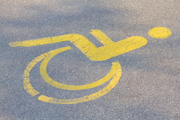 Yellow handicapped parking sign of a man on a wheelchair painted on the asphalt floor.
