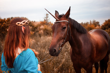 Fototapeta premium Beautiful young female elf with long dark wavy hair petting her horse resting in the woods forest nymph stroking her horse care pet love animals harmony caring owner gentle creature myth