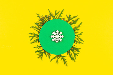 Christmas banner with coniferous tree branches and snowflake on yellow paper background. Round frame of Christmas tree branches and decorations with space for text. Top view. New year concept