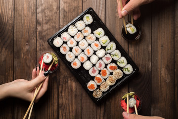 A plate of sushi rolls on a wooden table top view. Hands with chopsticks. Copy space. Traditional Asian cooking concept.