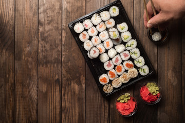 A plate of sushi rolls on a wooden table top view. Hands with chopsticks. Copy space. Traditional Asian cooking concept.