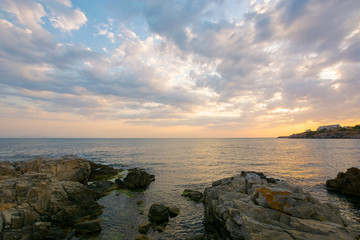 sunset at the coast of black sea. wonderful dramatic landscape with rocks on the pebble beach beneath a cloudy sky. velvet season vacations