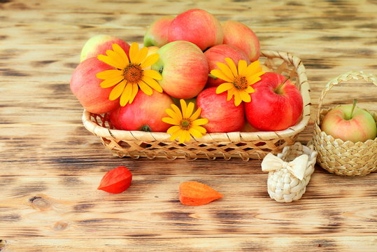Red ripe apples and autumn flowers lie in a wicker plate on a wooden table. Wicker bast shoes and apples in basket. Healthy food and lifestyle, vegetarianism.