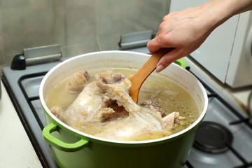 bone broth . A woman's hand is stirring the bone broth and cooking it in a large pot.