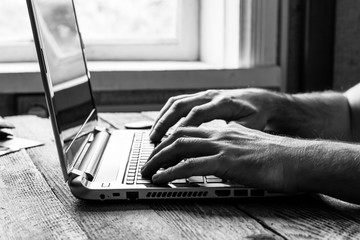 hands of a man working at a computer laptop at the window, black and white photo
