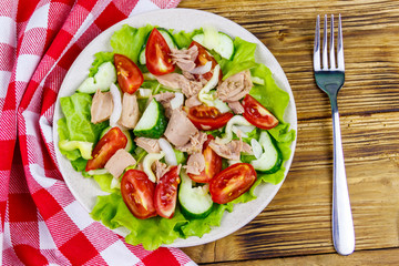Tasty tuna salad with lettuce and fresh vegetables on wooden table. Top view