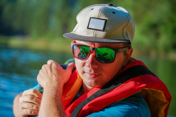 A portrait of a guy who is dressed in a life jacket with glasses and a cap on the background of the...