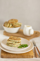 Zucchini pancakes with herbs on a light plate and a wooden board