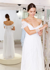 Naklejka premium Cheerful young woman dressed in luxury white gown standing in wedding shop