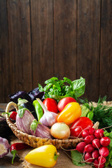 Assortment of vegetables in a basket on the table. A lot of different raw vegetables in the basket. Eggplant, tomatoes, garlic, sweet pepper, onion on the table. The concept of healthy eating