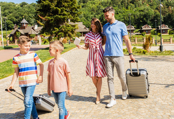 Smiling family of four going to the hotel to check in at the reception for vacation.