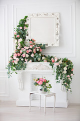 Fototapeta na wymiar Vertically, the interior of a white room decorated with pink flowers. White fireplace, mirror and flower garlands.