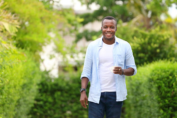 Naklejka na ściany i meble Healthy African American man holding a cup of coffee while walking in relaxation around the neighborhood with good green environment surrounding with copy space