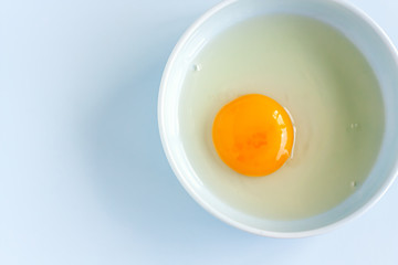 Fresh organic raw yolk and white of egg in light blue bowl on pastel background. Healthy breakfast and fresh ingredients. Selective focus. Top view. Space for text.