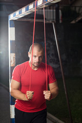 A man in a red t-shirt trains outside using a red resistance band.