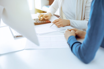 Accountant checking financial statement or counting by calculator income for tax form, hands close-up. Business woman sitting and working with colleague at the desk in office. Audit concept