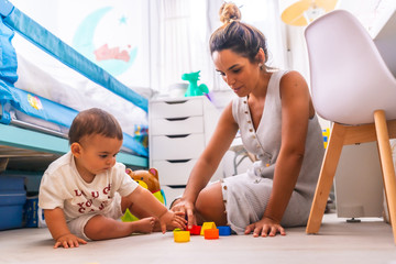 Young Caucasian mother playing with her in the room with toys. Baby less than a year learning the...
