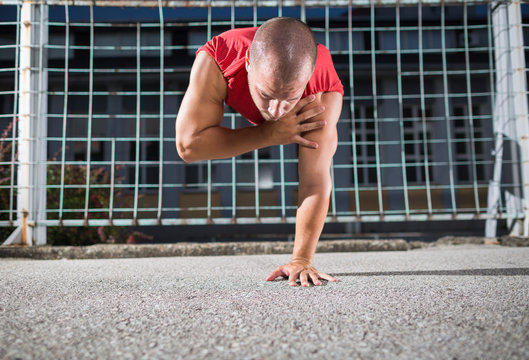 Athlete In A Red T-shirt Doing One Arm Handstand Push Ups At The Outdoor Gym.