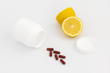 A plastic bottle for pills lies on the table, next to a brown capsule and pieces of lemon.