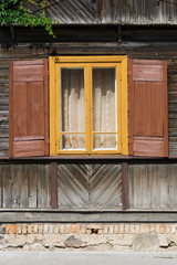 Wooden window rustic cottage house. Vintage wall with transparent glass window and decorative brown shutters. Pavement along house wall background. Countryside architecture historic building.