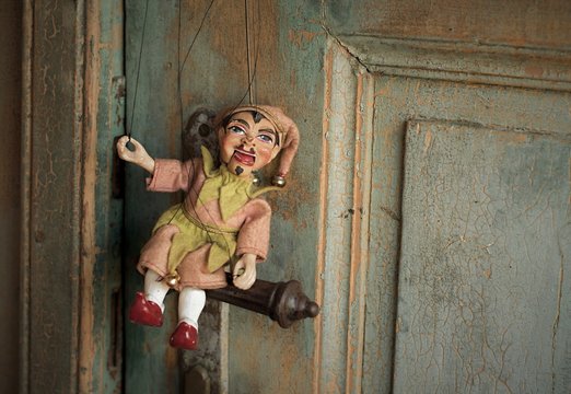 An Antique Traditional Puppet Laughing And Sitting On The Handle Of The Very Old Door  