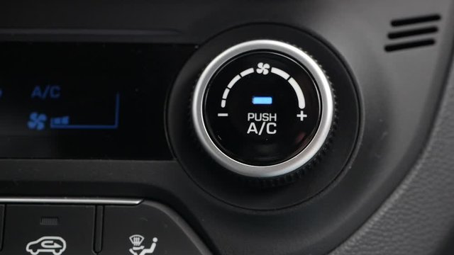 Close-up of pushing a button to turn on the air conditioner in a car. The mans hand turns the button