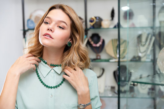 Stylish young female client choosing natural gemstone jewelry in boutique, trying on beads of polished green nephrite