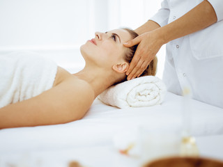 Young and blonde woman enjoying facial massage in spa salon. Beauty concept