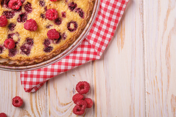 Sweet tasty pie with jellied and fresh raspberry fruits in baking dish with red tablecloth towel, wooden table background, top view close up