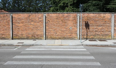 Surrounding brick wall, a concrete sidewalk, a crosswalk and a paved road ahead. Background for...