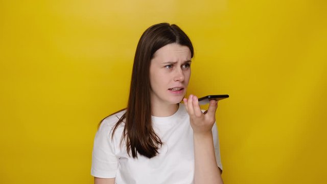 Angry young woman talking on smartphone, dissatisfied entrepreneur shouting when negotiating by mobile, isolated over yellow wall background in studio. People, lifestyle, emotions and stress concept