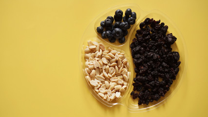 Berries ad nuts in round plastic container for food storage - yellow background