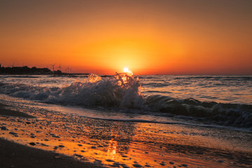 Fototapeta na wymiar sunrise at sea with waves and windmills on background
