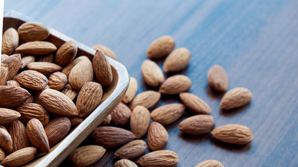 Almonds in small wooden bowl. Almonds laid freely on dark table. Row of bowls with almond nuts, top view. Peeled almond pattern