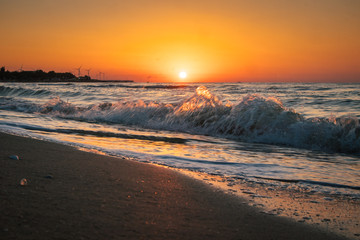sunrise at sea with waves and windmills on background