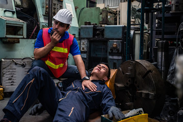 Asian man worker had accident unconscious on the floor at metal lathe factory. Male engineer supervisor talking on walkie talkie for help. Safety in Factory industrial and business insurance concept. - obrazy, fototapety, plakaty