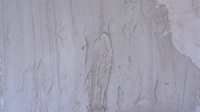 Plasterer man is spackling with putty plaster aligning wall with trowel, hands closeup. Finishing construction renovation works. Worker builder making overhaul applying plaster on wall using spatula.