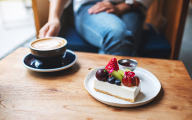 A woman drinking hot coffee and eating mixed fruits cheesecake in cafe