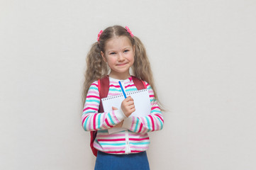 Back to school. Portrait of a blonde schoolgirl with a notebook and pen in her hands. She's surprised. Light grey Studio background. Education. Preparation for school. place to copy.