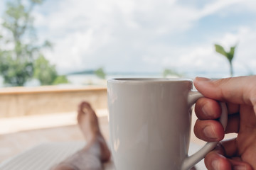 Man drinks coffee on the balcony by the sea in concept of relaxation and vacation.