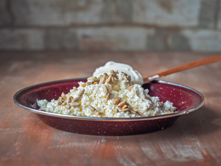 Light breakfast with cottage cheese, sour cream and sunflower seeds on a flat brown ratelka with a wooden spoon