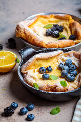 Dutch baby pancake with berries and lemon in cast iron frying pan.
