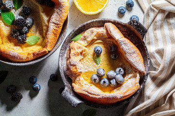 Dutch baby pancake with berries and lemon in cast iron frying pan, top view.