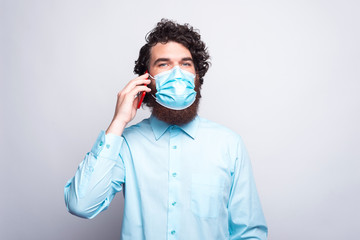 Photo of casual man talking on phone and wearing medicinal mask.