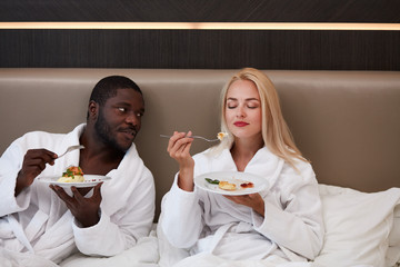 adorable multiethnic couple have breakfast in hotel, they have tasty meal together, enjoy, relax, happy weekends. on bed