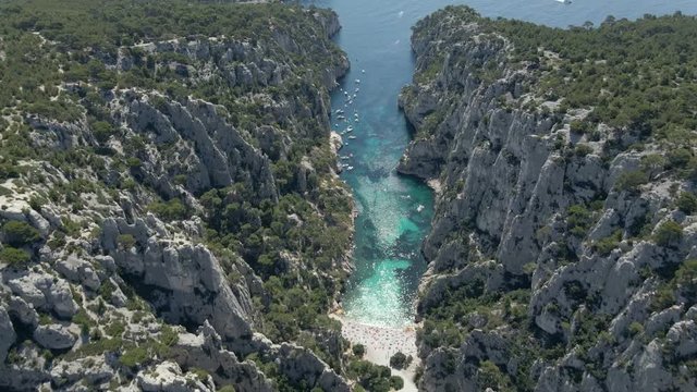 Aerial view of En Vau calanque next to Cassis in France with boats, trees, cliffs and people on a small rocky beach